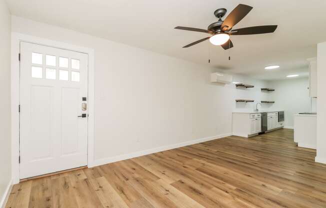 an empty living room with a ceiling fan and a kitchen in the background