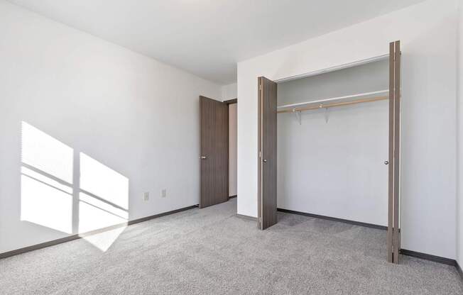 A room with a carpeted floor, a white wall, a wooden door, and a white closet with a metal rod.