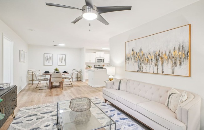 A living room with a white couch, a glass coffee table, and a painting on the wall.