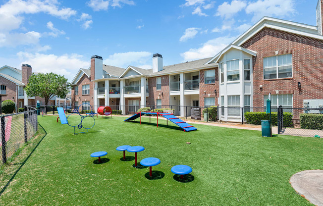 A playground area with blue and green equipment is surrounded by apartment buildings.