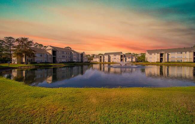 A serene landscape with a lake, grass, and buildings in the background.