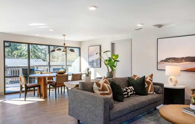 A modern living room with a grey couch and a dining table with chairs.