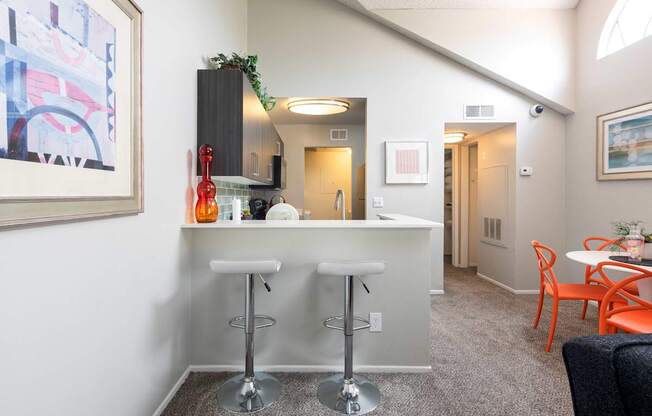 a bar with three stools in a living room with a kitchen and a hallway