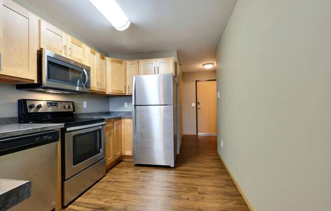 an empty kitchen with stainless steel appliances and wooden cabinets. Fargo, ND Urban Plains Apartments