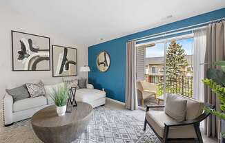 A living room with a white couch, a coffee table, and a large window with a view of a house and trees outside.