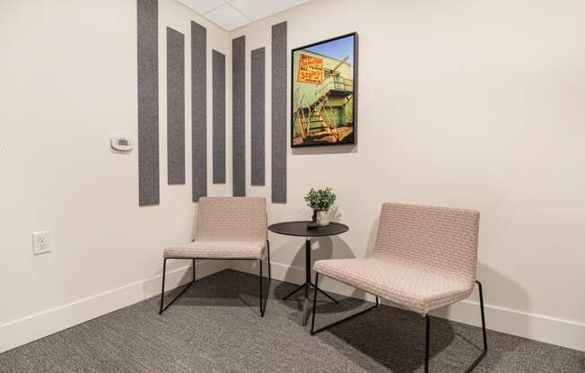 two chairs and a table in a room with a painting on the wall