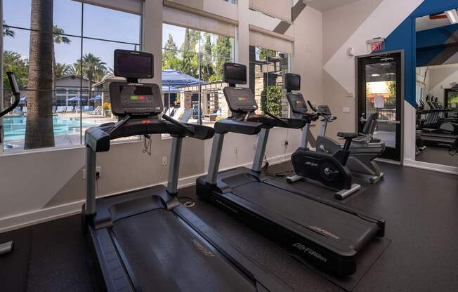 A treadmill in a gym with a view of the pool outside.