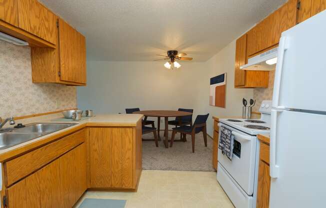 Fargo, ND Sugarplum Apartments. A kitchen and dining room. The dining room has a table with four chairs around it with a ceiling fan and light directly above it.