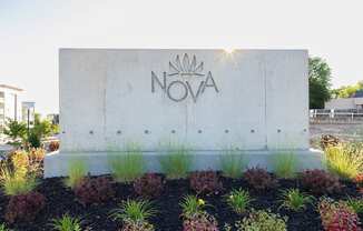 A concrete sign with the word NOVA on it is surrounded by plants.