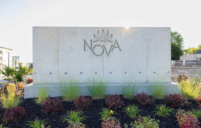 A concrete sign with the word NOVA on it is surrounded by plants.