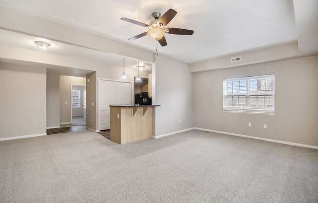 An enlarged living room with a carpeted floor, a ceiling fan, and a window with blinds at Lynbrook Apartments and Townhomes, Elkhorn, NE, 68022