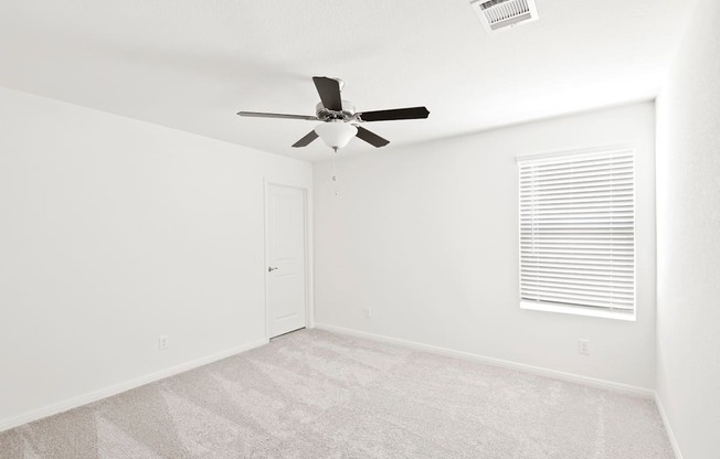 a bedroom with a window, white walls and a ceiling fan