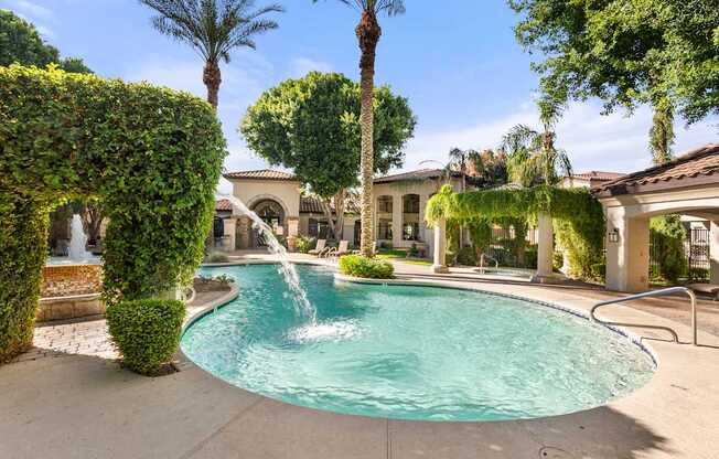 A pool with a waterfall surrounded by green plants and trees.