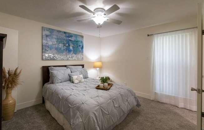 A bedroom with a bed, white ceiling fan, and a painting on the wall in a 1 bedroom, 1 bath 554 sq ft apartment home at The Biltmore Apartments located in the Vickery Midtown neighborhood of Dallas, TX.