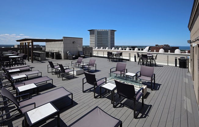 A rooftop patio with chairs and tables overlooking a cityscape.