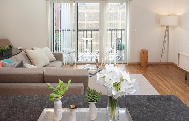 A living room with a grey couch and a table with a vase of white flowers on it.