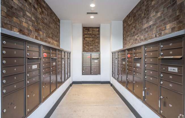 A long hallway with a brick wall and mailboxes on the side.