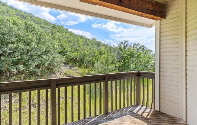 A wooden deck with a railing overlooks a green hillside.