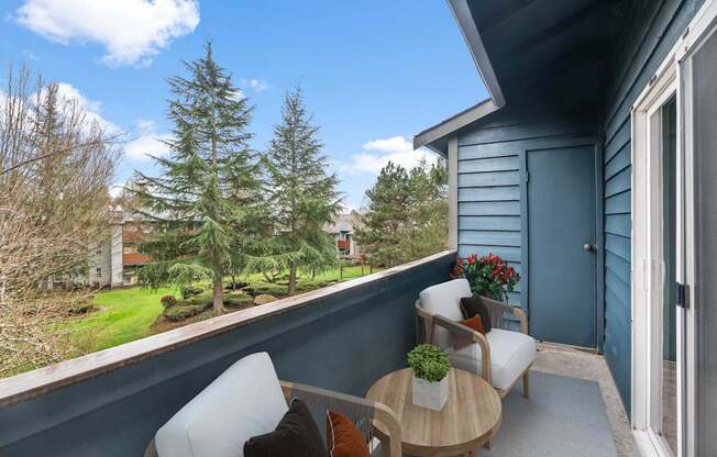 A balcony with a table and chairs overlooking a garden.