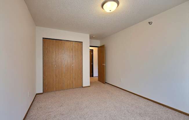 A spacious living room with carpet and a door to a bedroom. Fargo, ND Eagle Run Apartments.