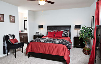 A bedroom with a red bedspread and a black chair.