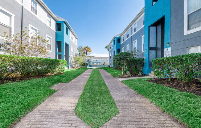 a walkway between two apartment buildings with green grass and bushes on either side