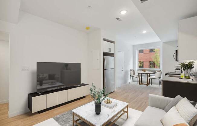 Contemporary living room with a neutral color scheme, featuring a sleek TV unit, comfortable white sofa, and an integrated dining area visible in the background.