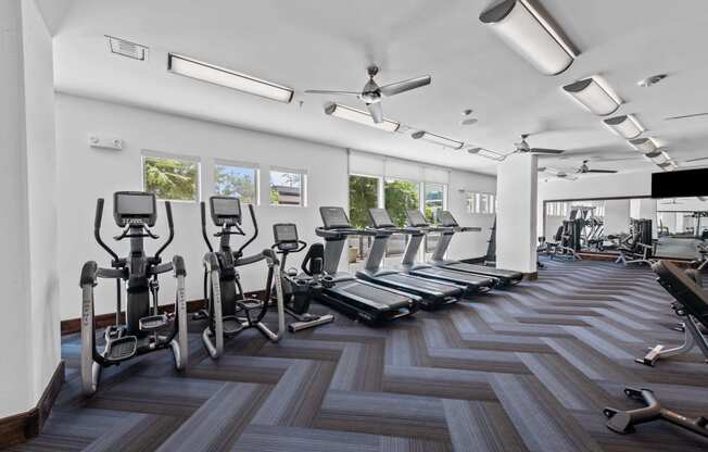 a gym with cardio machines and a tv