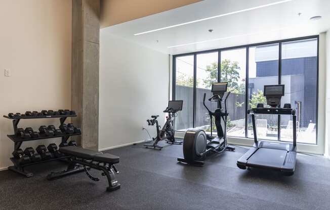 a gym with weights and cardio equipment in a room with large windows at Analog PDX Apartments, Portland, OR 97227