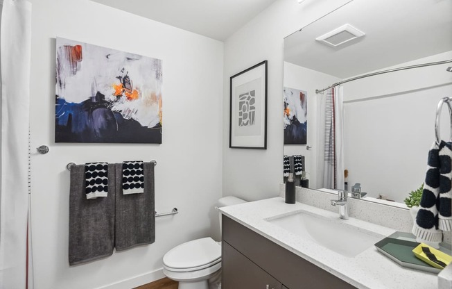 A bathroom with a toilet, sink, and a painting on the wall.