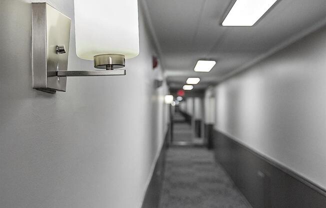 a long narrow hallway with lights on the wall and a carpeted floor at Troy Place Apartments - Troy, MI, Troy