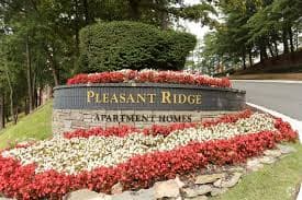 a stone sign with red and white flowers on the side of a road
