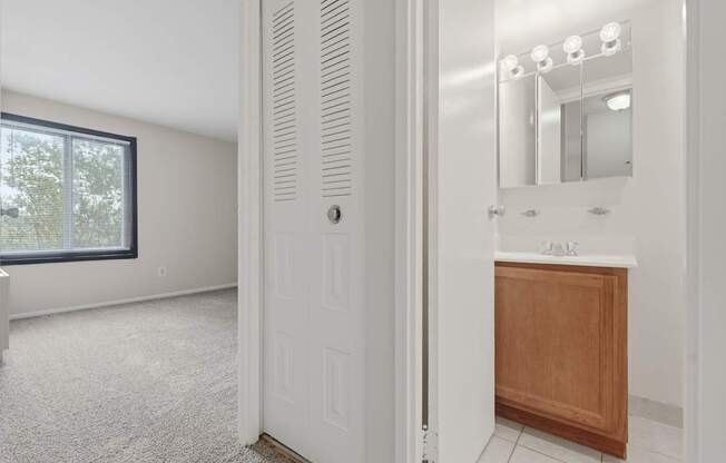 A white door is open to a bathroom with a sink and mirror.