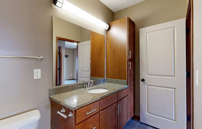 a bathroom with a granite sink vanity, a mirror, and overhead lighting