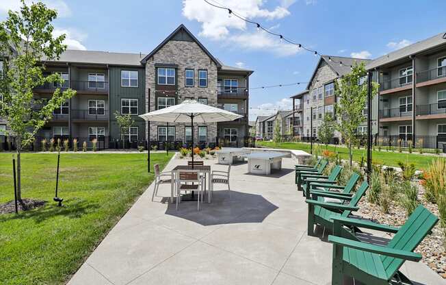 an outdoor patio with tables and chairs and an umbrella in front of an apartment building at The Depot Raymore, MO 64083