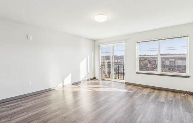 A spacious room with wooden floors and a view of the city through the windows.
