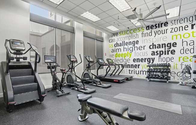 A gym with a variety of equipment and a motivational word cloud on the wall.