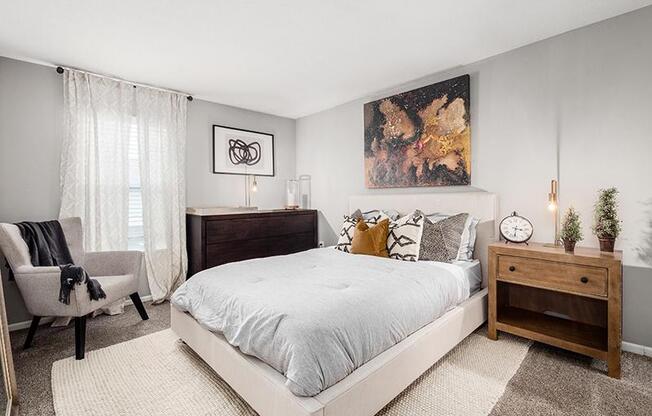 A bedroom with a large bed, a chair, and a painting on the wall.