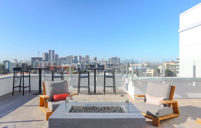 a rooftop terrace with chairs and a fire pit and a city in the background