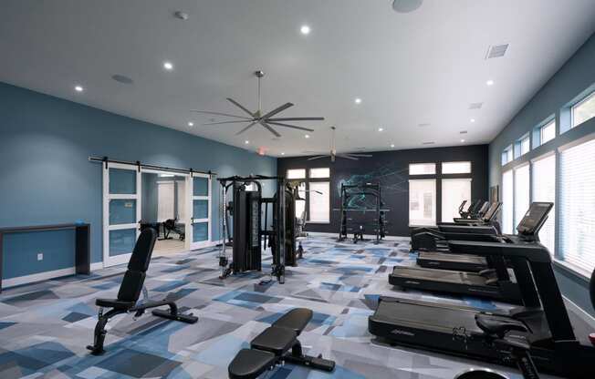 a gym with weights and cardio equipment in a large room with windows