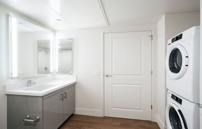 Bathroom with full-sized front loading washer dryer, backlit mirror and stunning vanities