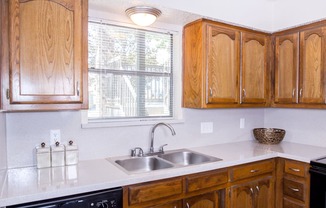 Model kitchen with a sink, wooden cabinets, and a window at Chisholm Place Apartments in Plano, TX