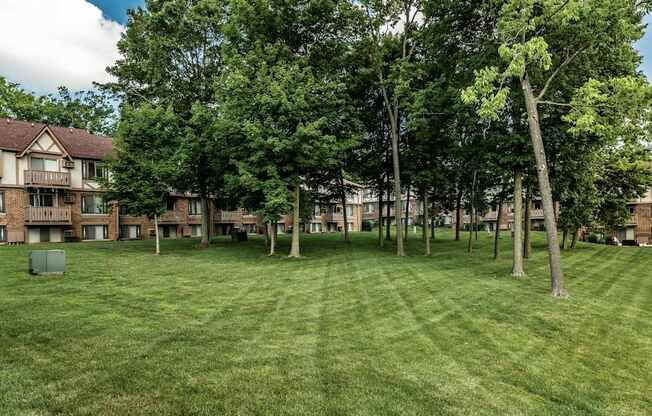 A grassy field with trees and apartment buildings in the background