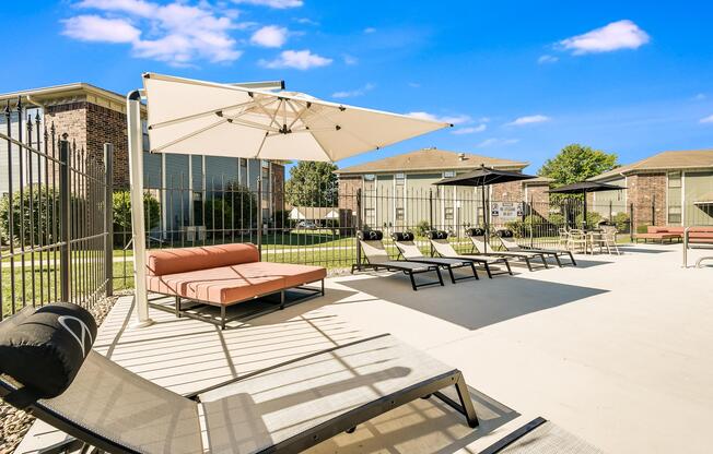 Tanning chairs and umbrellas in poolside lounge area at The Arbor in Blue Springs, Missouri 