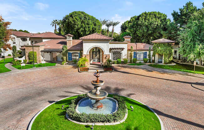 A fountain in the middle of a paved area with a house in the background.