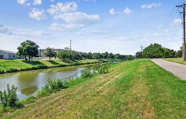 A serene landscape with a river, green grass, and a clear sky. at The Canyons Apartments, Fort Worth