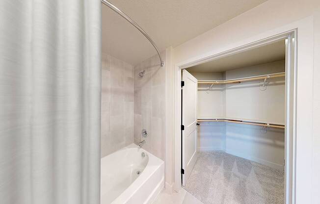 A white bathroom with a tub and a walk in closet.