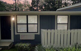 A house with a white picket fence and green plants in front.
