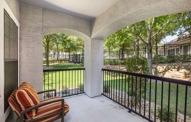 A patio with a striped chair and a view of a fenced yard.