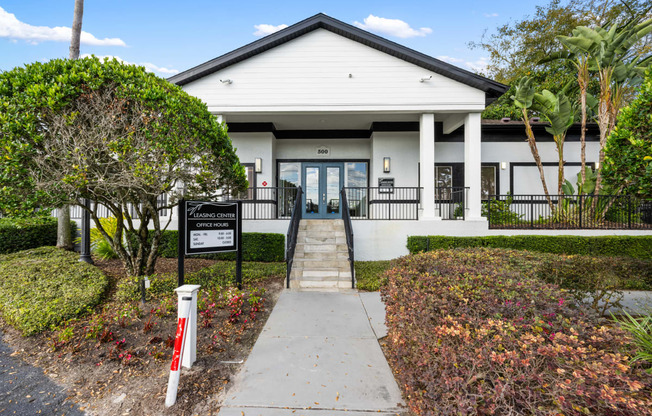 the front of a white building with a sidewalk and a black sign